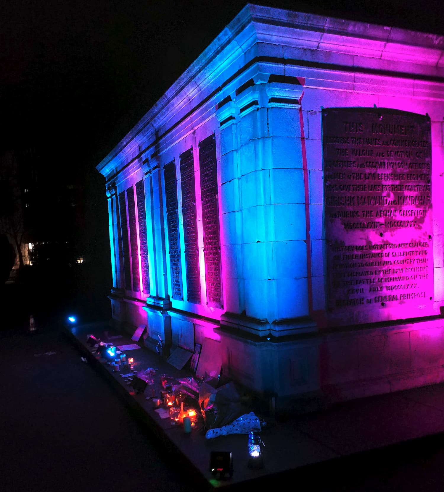 The plinth of the lion statue with candles at its base, lit up in trans colors